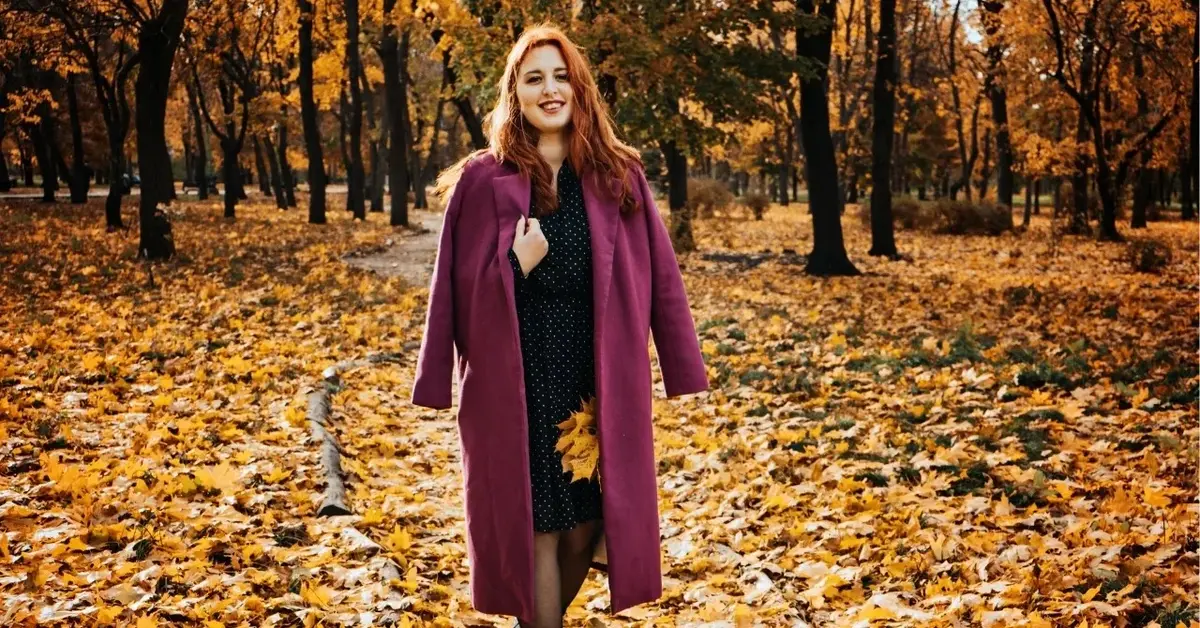 dziewczyna w płaszczu z rudymi włosami wśród jesiennych liści w parku