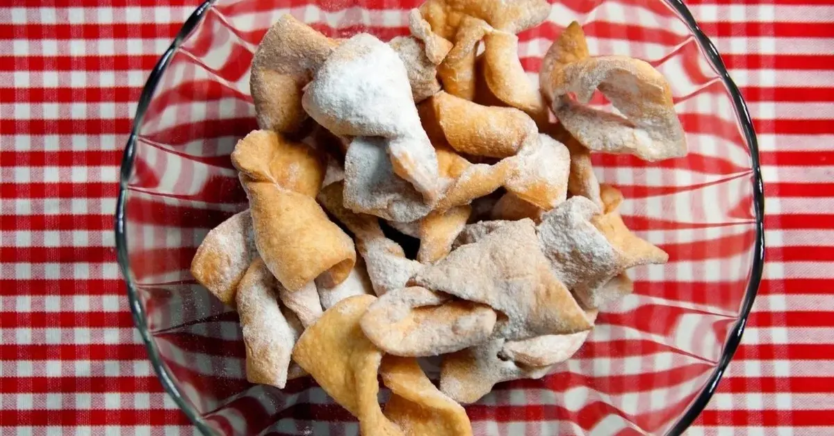 faworki w szklanej misce posypane cukrem pudrem na kratowanym obrusie