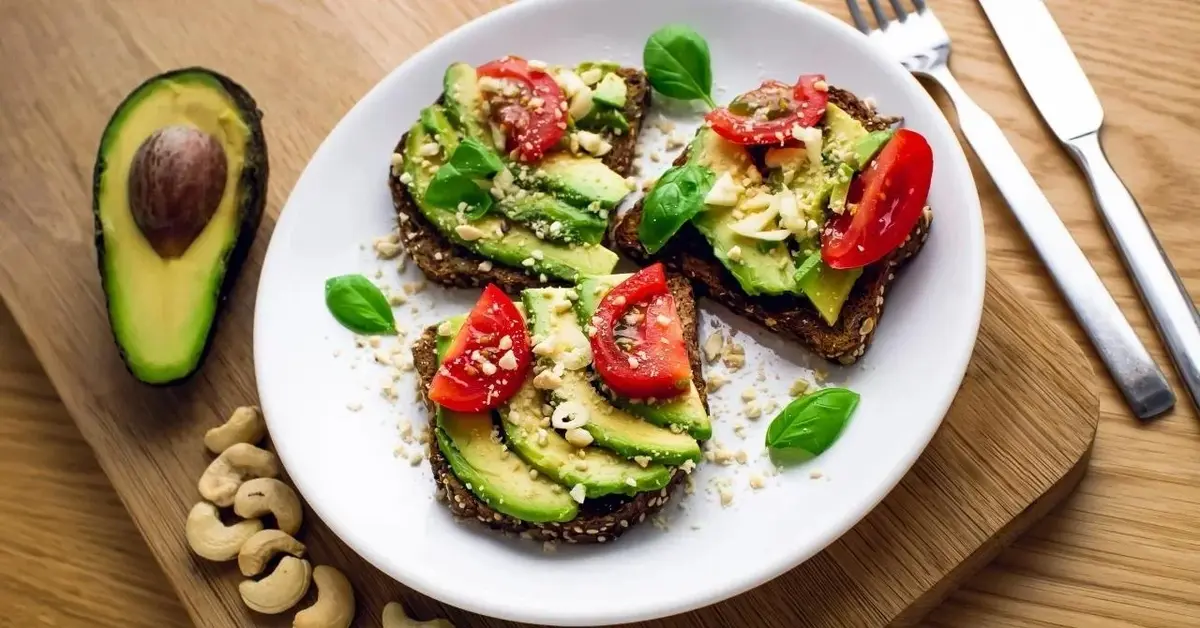 Kanapka z awokado i pomidorkami. Obok leży widelec.