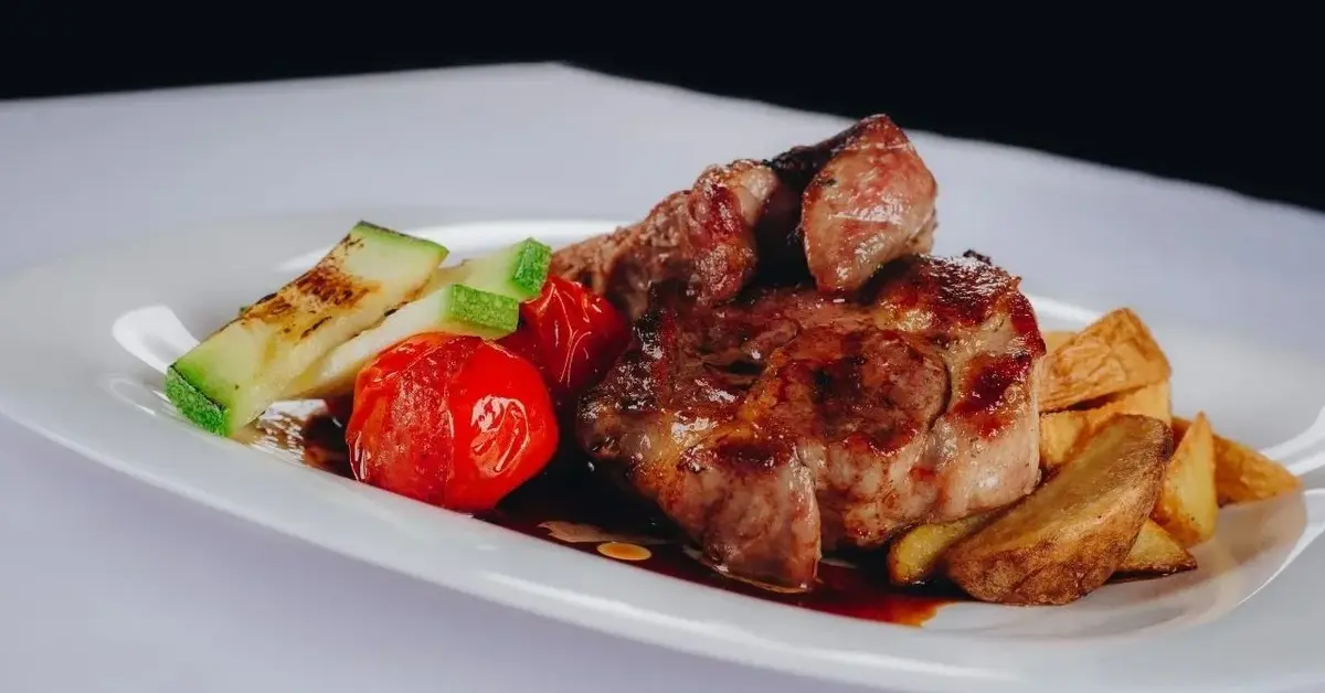 Karkówka w piwie na talerzu z pieczonymi warzywami.