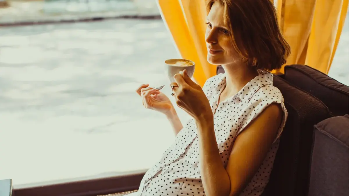 kobieta w ciąży siedzi z kubkiem kawy w ręku