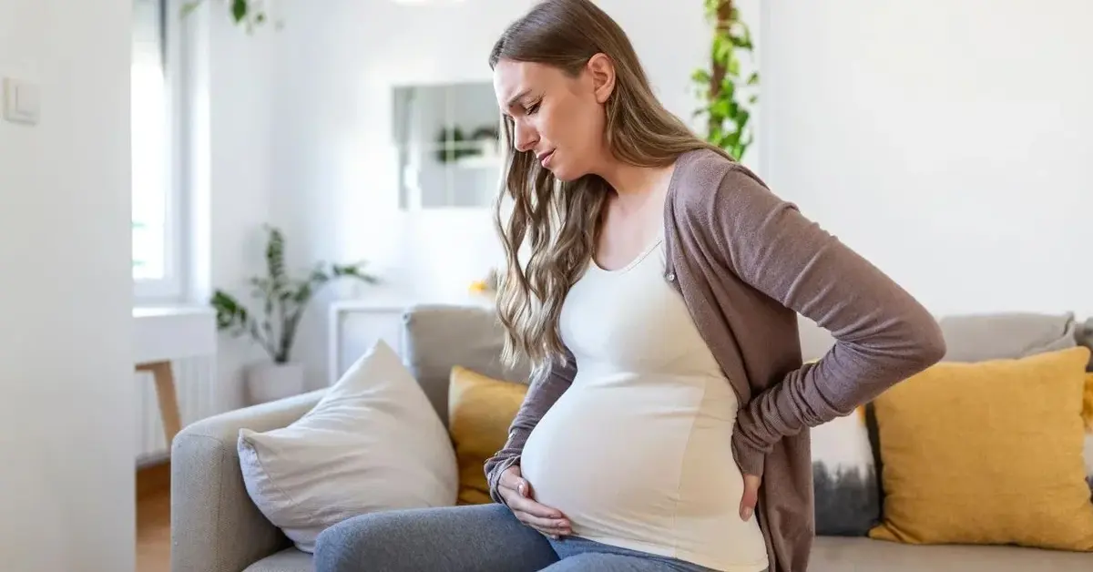 Kobieta w ciąży cierpiąca na kłopotliwe wzdęcia w ciąży siedzi skulona na kanapie