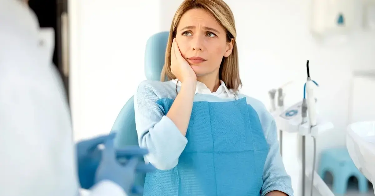 Kobieta u dentysty trzyma się za twarz. Czuje ból przez zębodół.