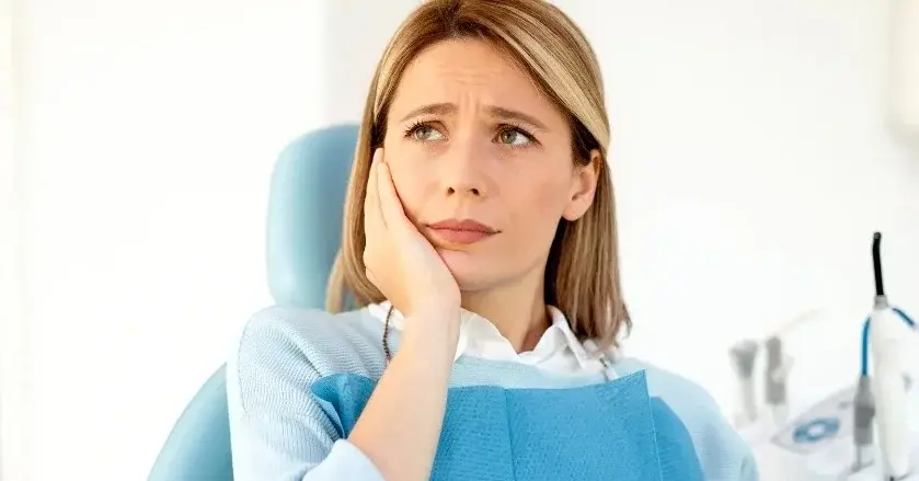 Kobieta u dentysty trzyma się za twarz. Czuje ból przez zębodół.
