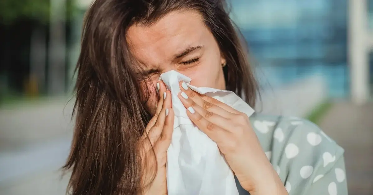 Kobieta ma katar i dmucha nos w chusteczkę.