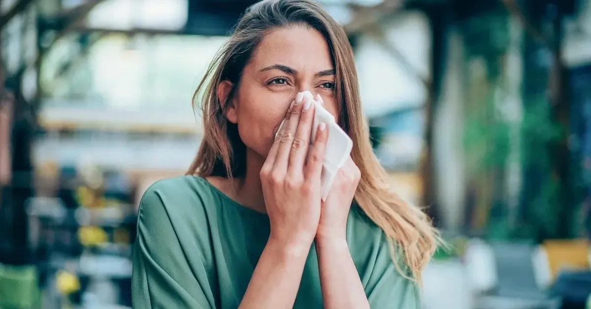 Kobieta otoczona przez zieleń kicha, bo ma uczulenie na zarodniki grzybów.