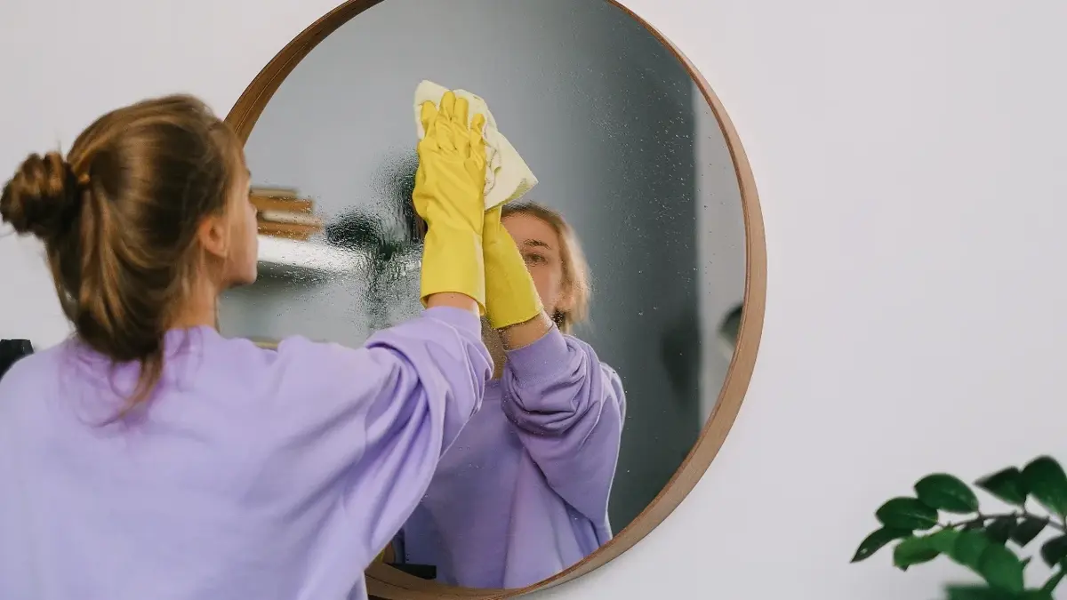 Kobieta w gumowych rękawiczkach myje lustro.