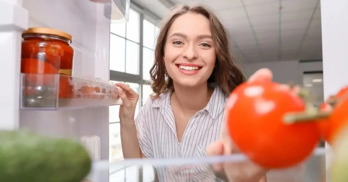 Kobieta się uśmiecha i przechowuje jedzenie w lodówce.