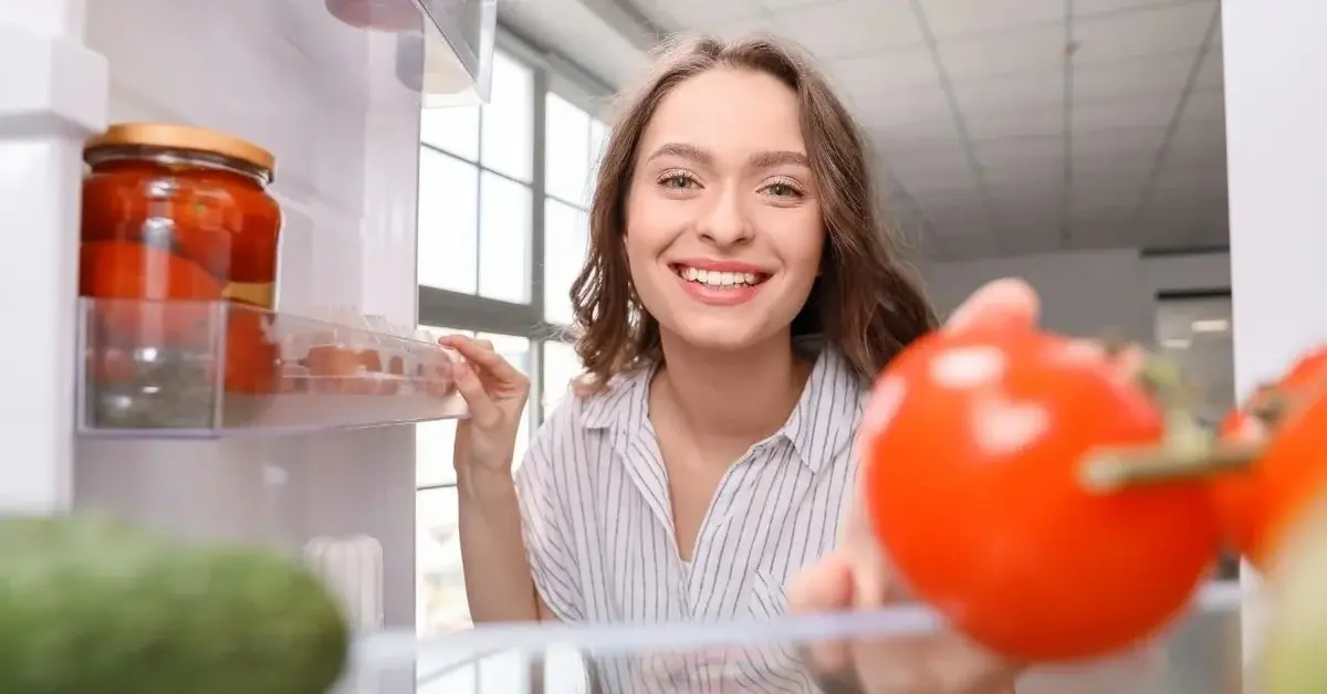 Kobieta się uśmiecha i przechowuje jedzenie w lodówce.