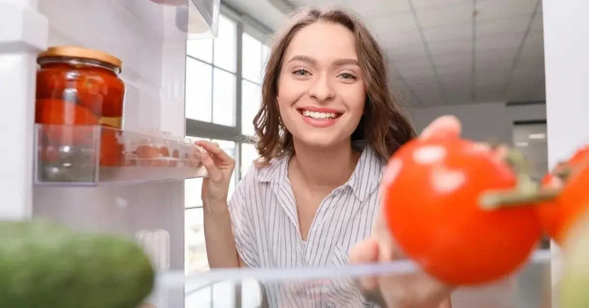 Kobieta się uśmiecha i przechowuje jedzenie w lodówce.