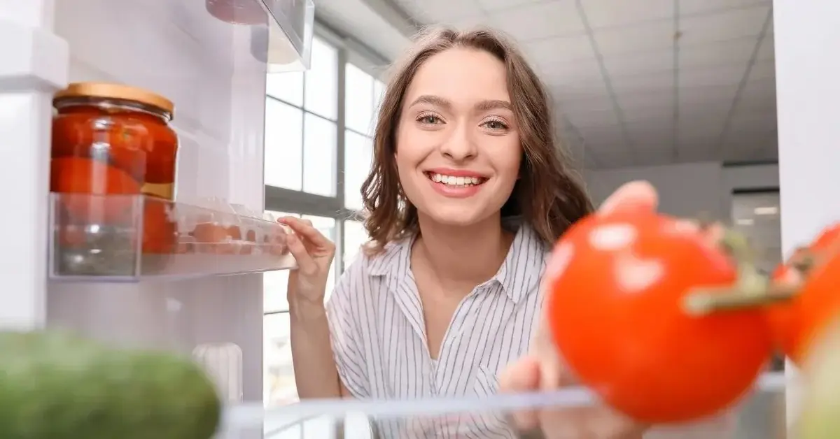Kobieta się uśmiecha i przechowuje jedzenie w lodówce.