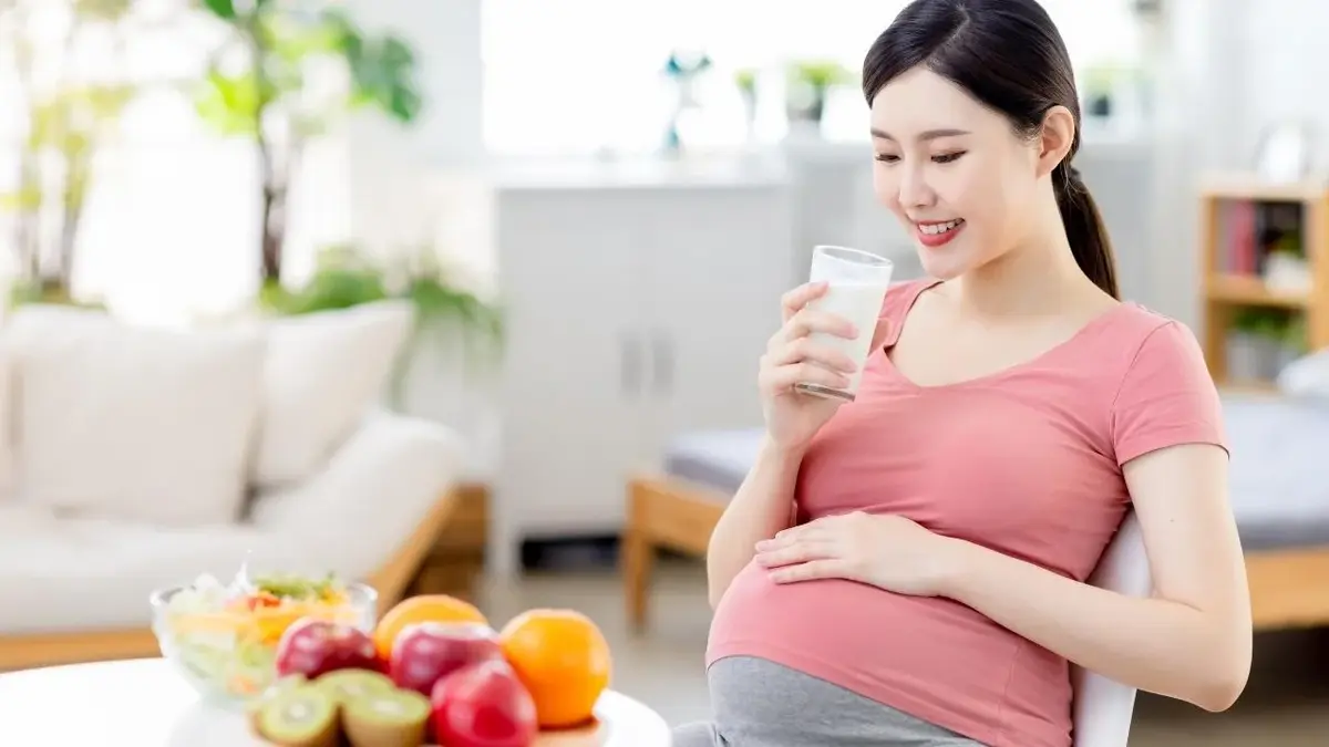 Uśmiechnięta kobieta w ciąży pije mleko ze szklanki na zgagę.