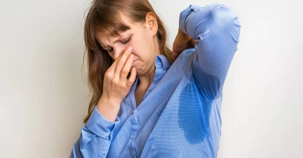 Kobieta w niebieskiej koszuli zatyka nos, bo bardzo spociła się pod pachami.