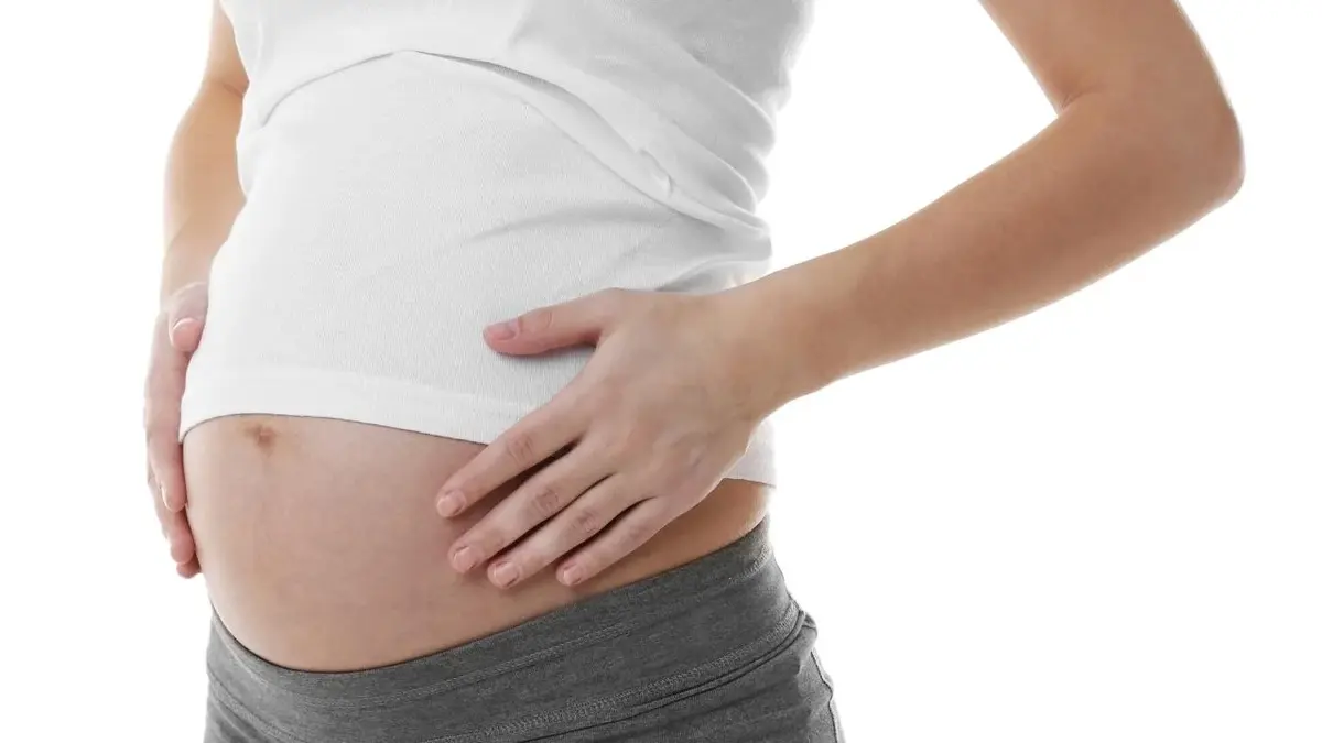 Kobieta we wczesnej ciąży ma widoczny brzuch ciążowy.