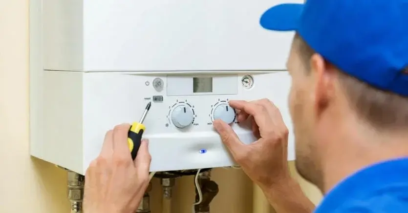 Fachowiec w niebieskim roboczym ubraniu montuje kocioł gazowy