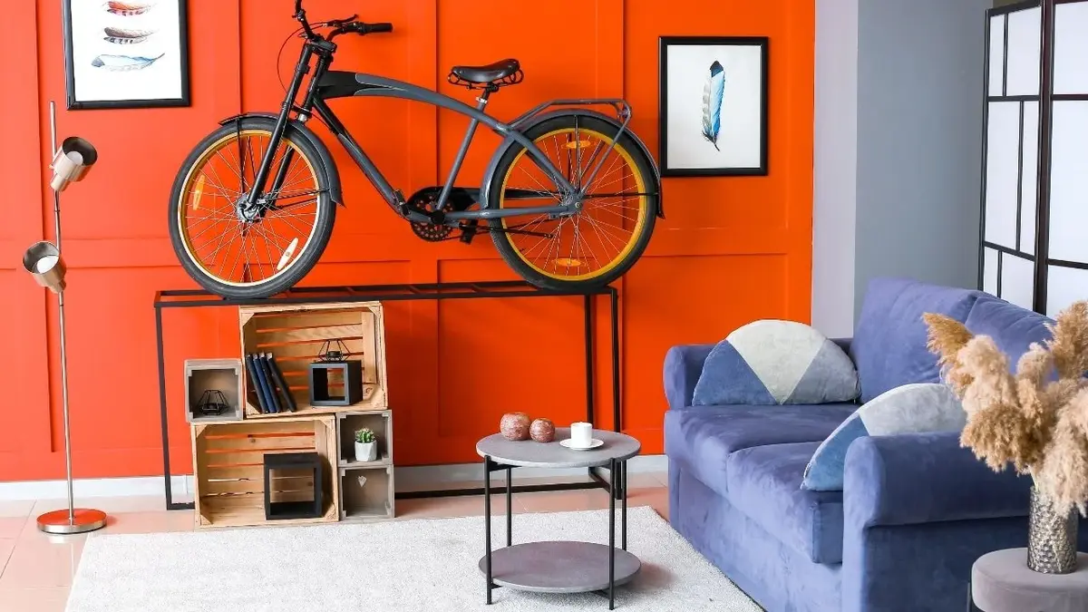 Salon z pomarańczową ścianą, czarnym rowerem, granatową kanapą i szarym dywanem