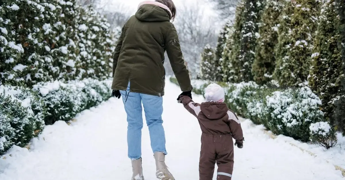 Rodzic z małym dzieckiem w kombinezonie zimowym dla malucha w lesie zasypanym śniegiem