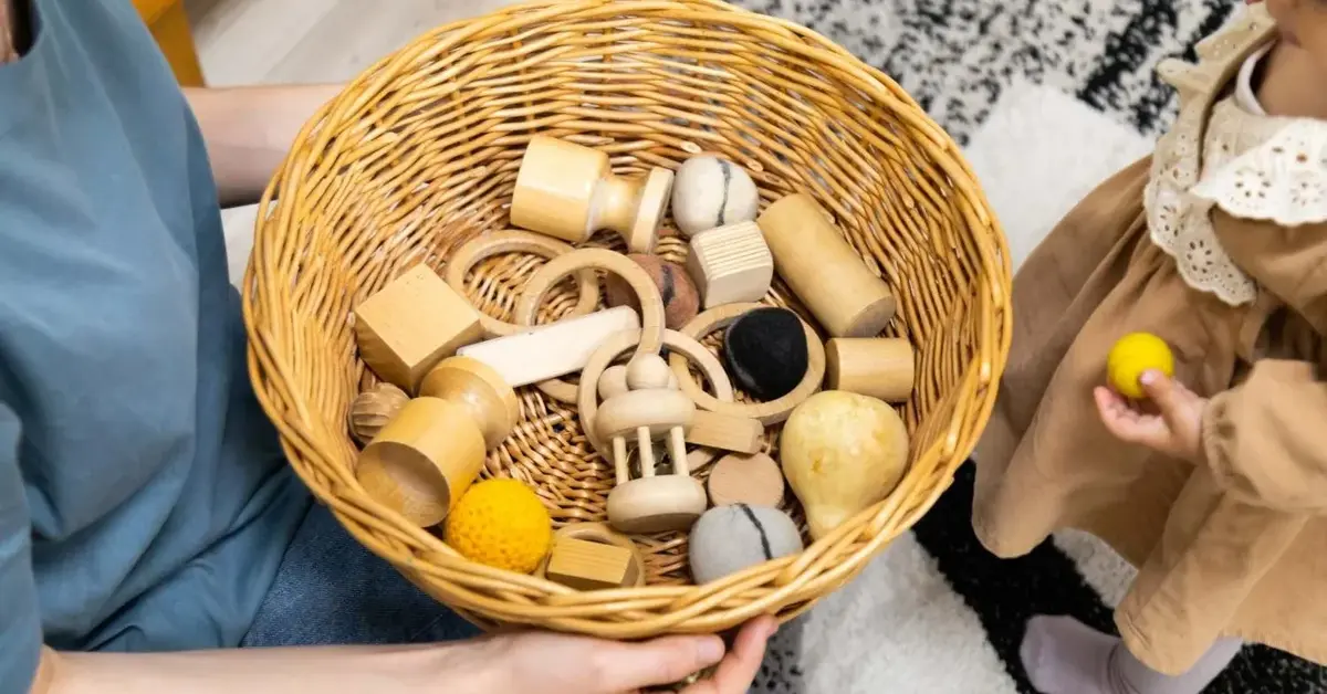 W dziecięcych rękach kosz wiklinowy na zabawki pełen drewnianych klocków