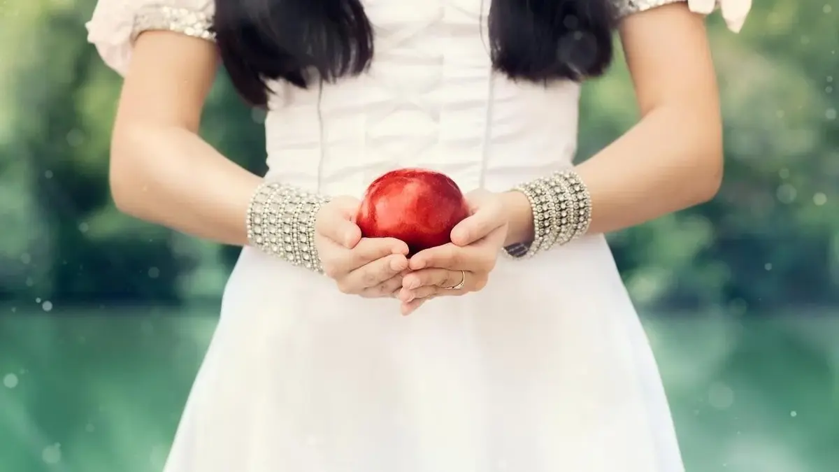 Królewna Śnieżka z baśni dla dzieci trzyma w ręku czerwone jabłko.