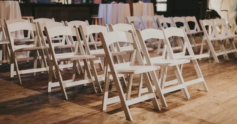 Kilka rzędów jasnych drewnianych krzeseł składanych w dużej sali o drewnianej podłodze