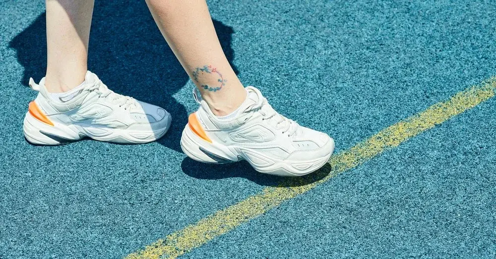 Kobiece stopy w masywnych białych sportowych butach przekraczają linię na bieżni