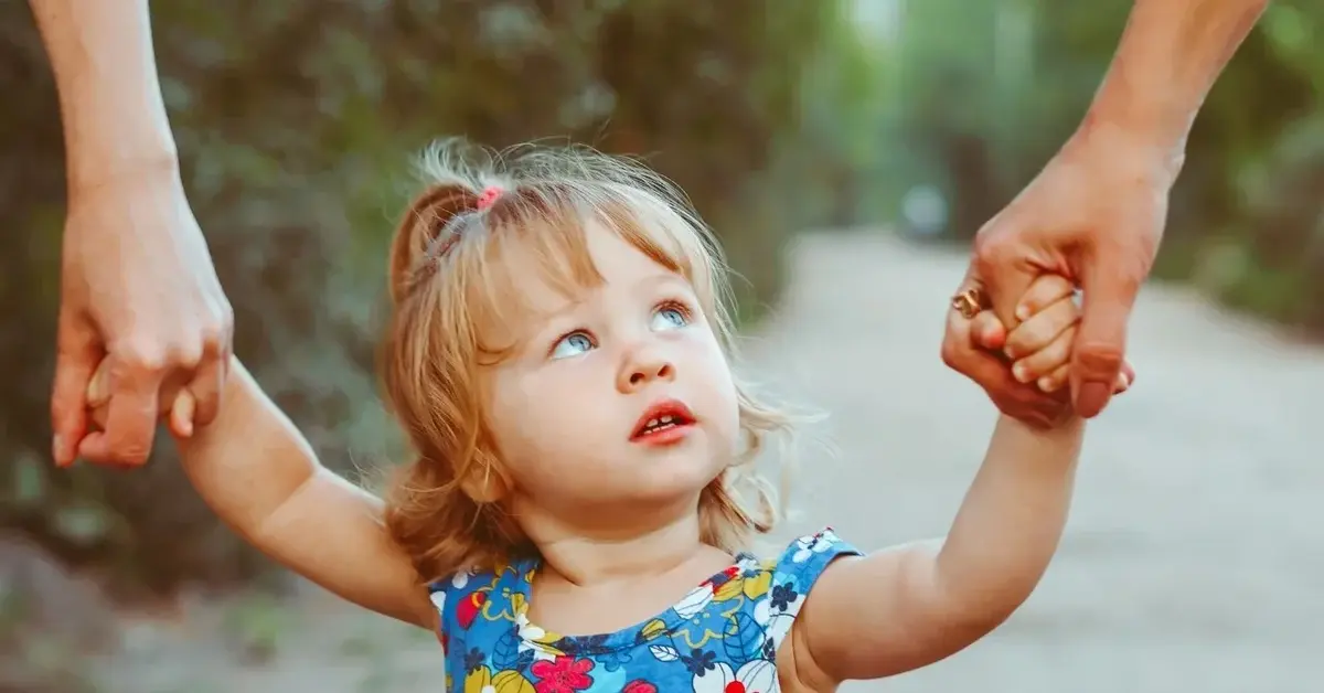 dziewczynka trzyma dłonie rodziców i patrzy do góry lęk separacyjny dziecka