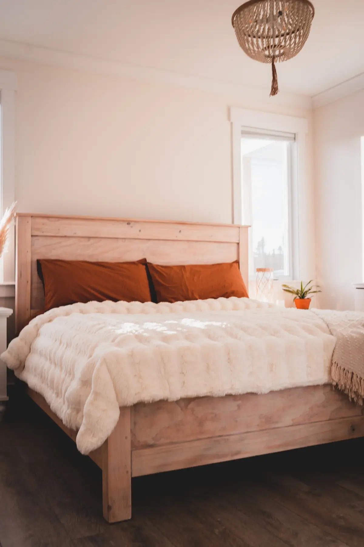 Łoże drewniane w przytulnej sypialni w jasnych kolorach z pomarańczowymi poduszkami i jasną narzutą