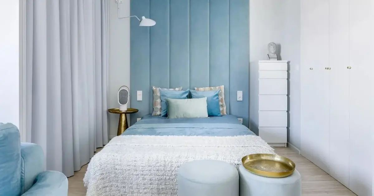 Sypialnia utrzymana w kolorach białym i błękitnym z dużym tapicerowanym łóżkiem pośrodku