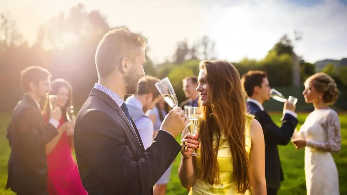 Młodzi ludzie w kolorowych strojach piją szampana na weselu.