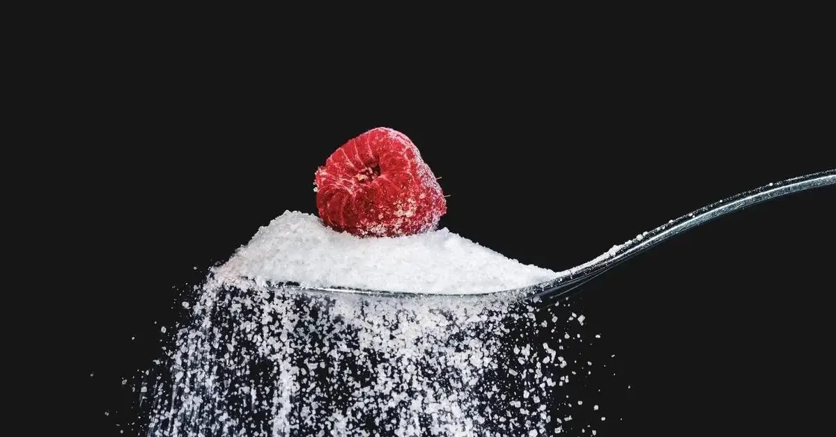 Łyżka z której sypie się cukier, a na cukrze leży malina.