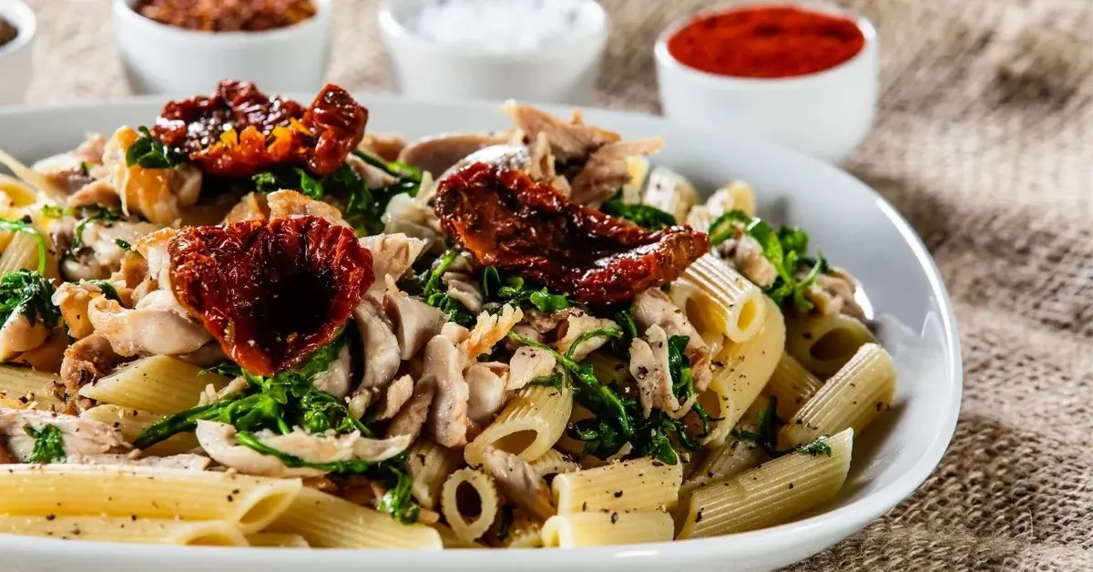 makaron z kurczakiem i suszonymi pomidorami w talerzu z tyłu przyprawy w  miseczkach