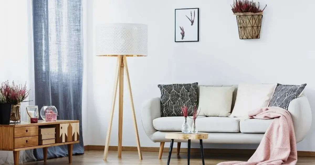 Mały salon w bloku z szarą kanapą, drewnianą szafką i lampą podłogową