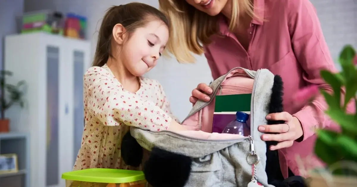 Kobieta pomaga dziewczynce spakować plecak do szkoły.