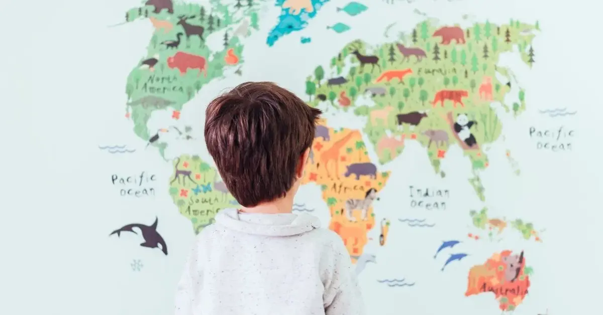 Chłopczyk o ciemnych włosach stoi przed wielką mapą świata na ścianę