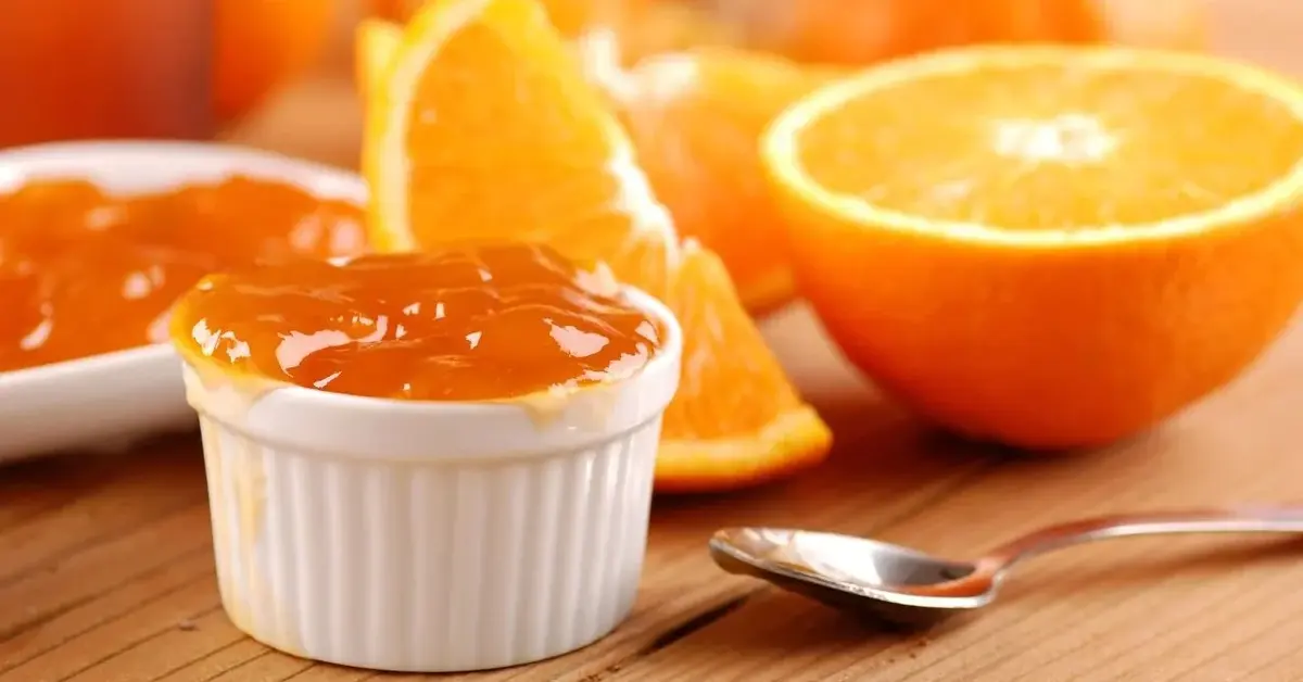 Marmolada pomarańczowa w białej miseczce, obok świeże pomarańcze