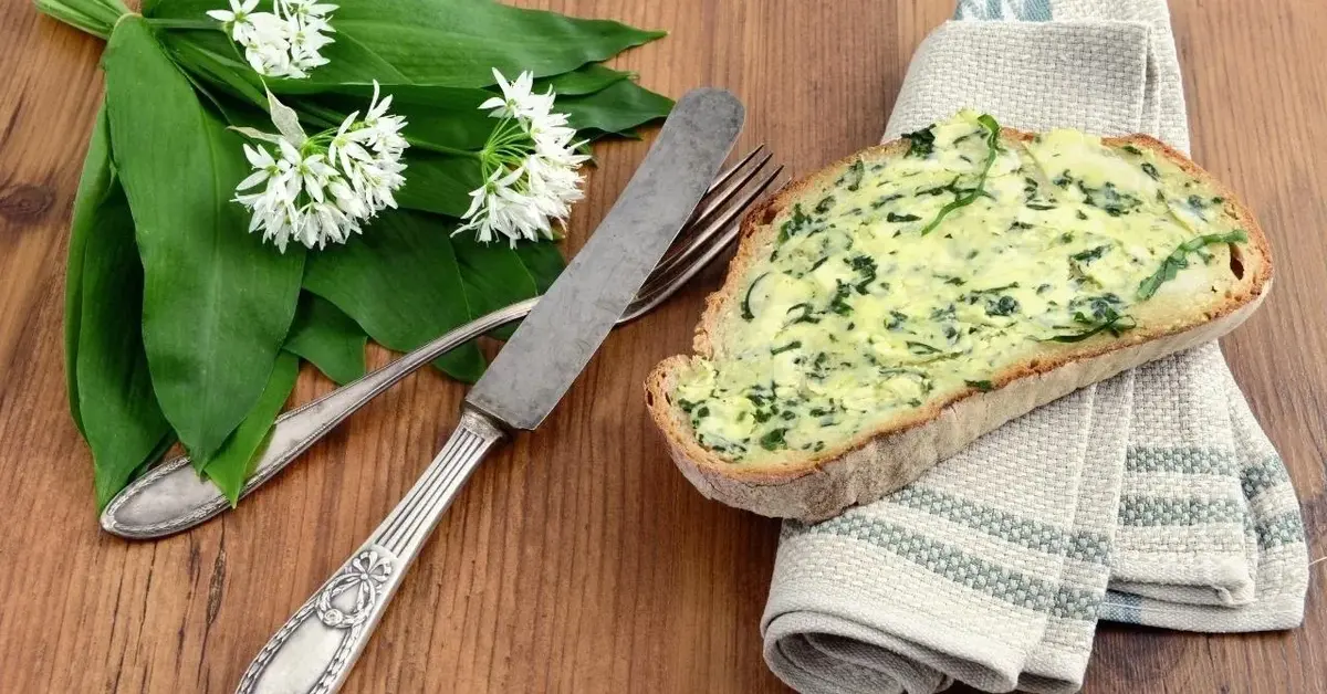 Chleb z masłem czosnkowym. Obok jest pęczek czosnku niedźwiedziego.