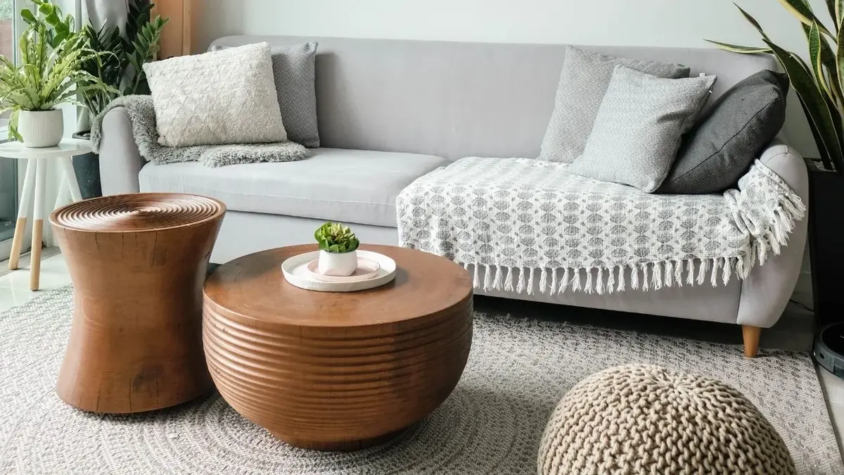 Dwa okrągłe stoliki kawowe w kolorze miedzi jako statement piece koło szarej kanapy z szarymi poduszkami