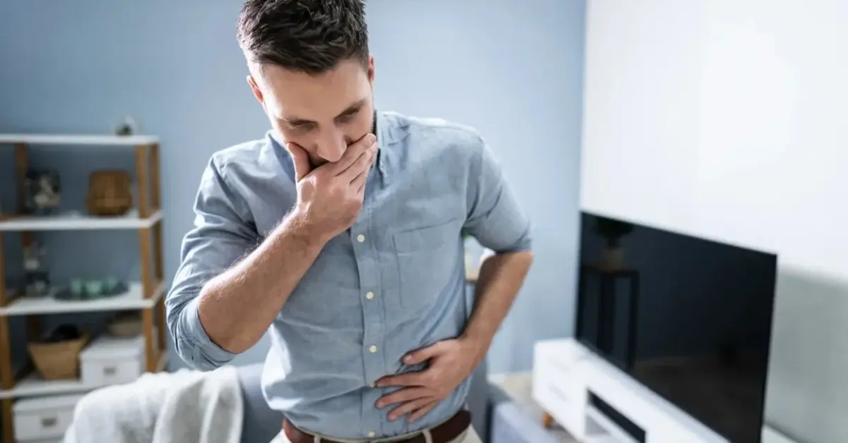 Mężczyzna trzyma się za żołądek bo ma mdłości po jedzeniu.