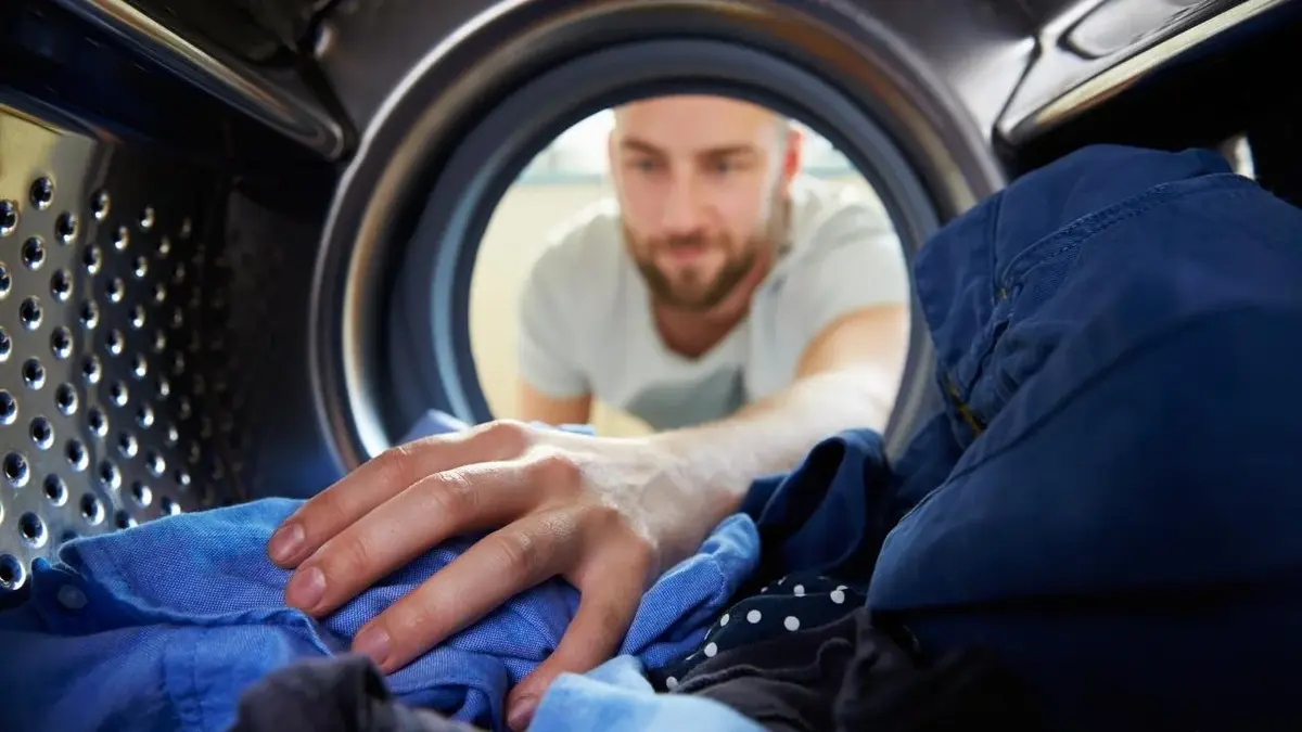 Mężczyzna stosuje domowe sposoby przy praniu w pralce.
