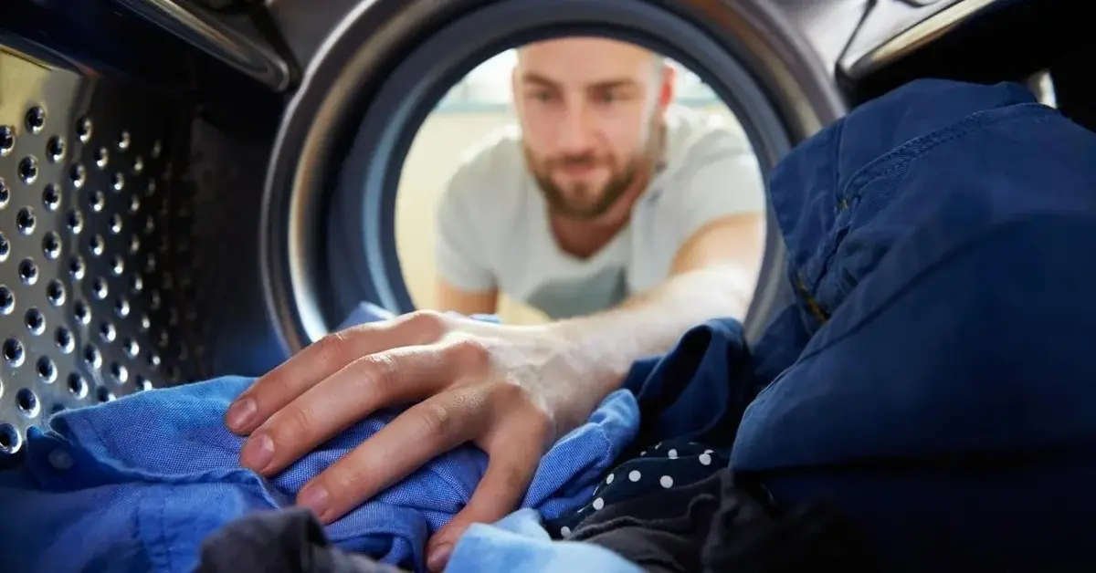 Mężczyzna stosuje domowe sposoby przy praniu w pralce.