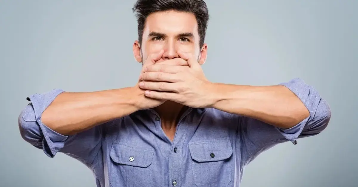 Mężczyzna zasłania rękami usta, które bolą go przez afty.