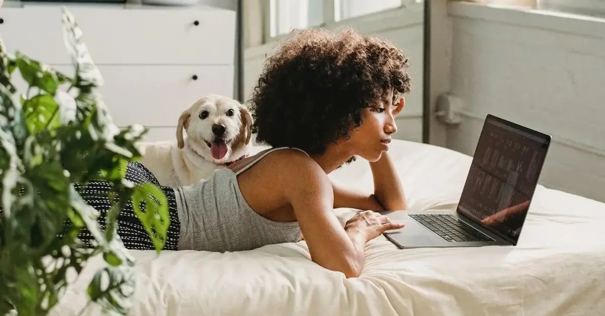 Kobieta z burzą kręconych włosów leży obok psa na łóżku w przytulnym pokoju w wygodnym domowym ubraniu