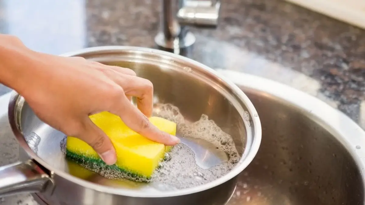 Jak wymyć przypalony garnek - kobieta myje rondel płynem pod bieżącą wodą 