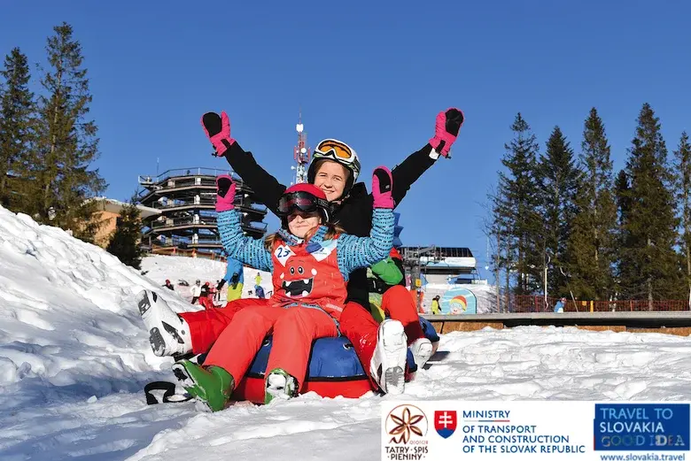 Słowacja Pieniny Spisz na tle ścieżki w koronach drzew rodzina w strojach narciarskich zjeżdża szybkimi sankami