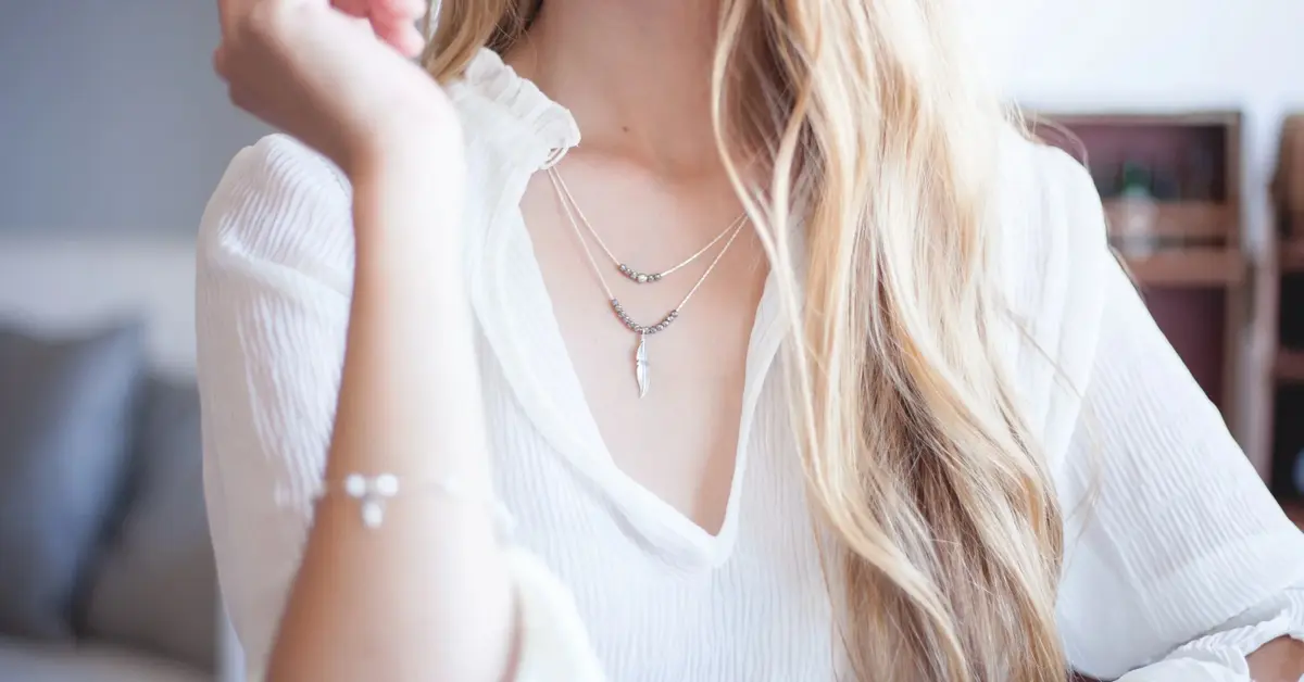 Kobica sylwetka z widocznym tułowiem w białej koszuli oraz rozpuszczonymi blond włosami, a na szyi naszyjnik z grawerem