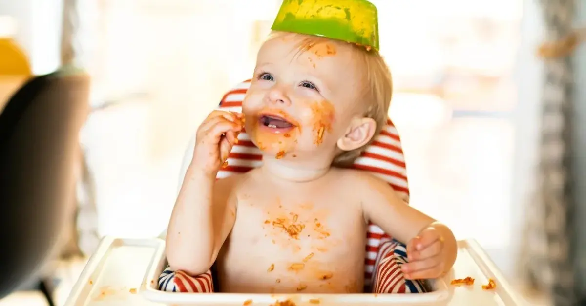 niemowlę wybrudzone jedzeniem uśmiechnięte z miską na głowie