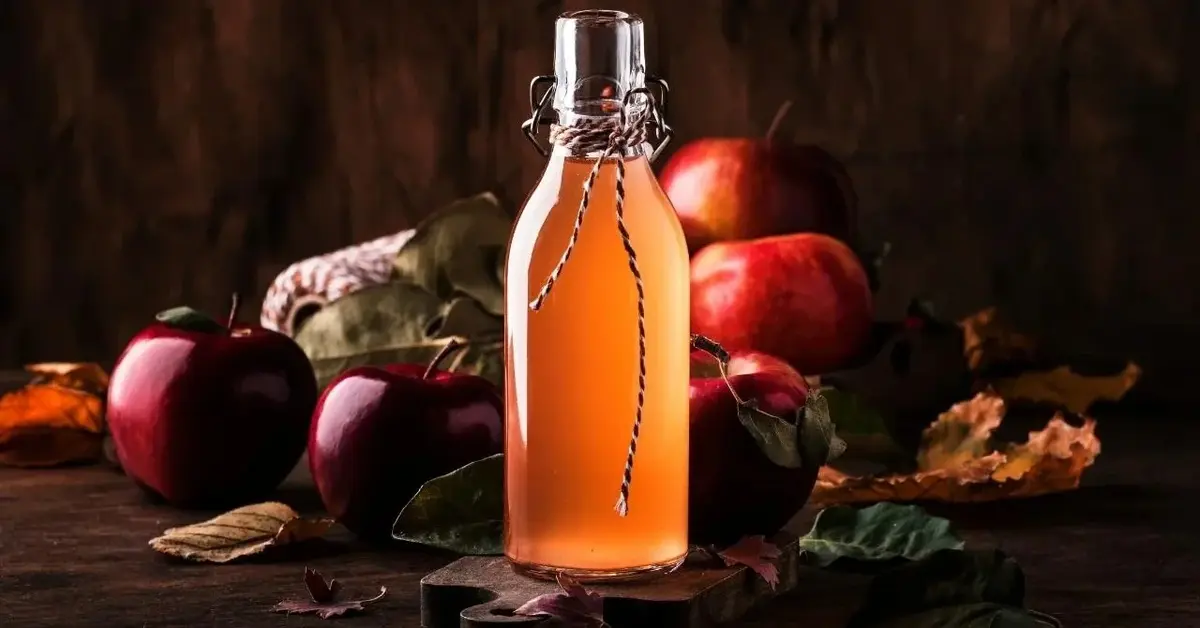 Ocet jabłkowy na tle czerwonych jabłek i jesiennych liści.
