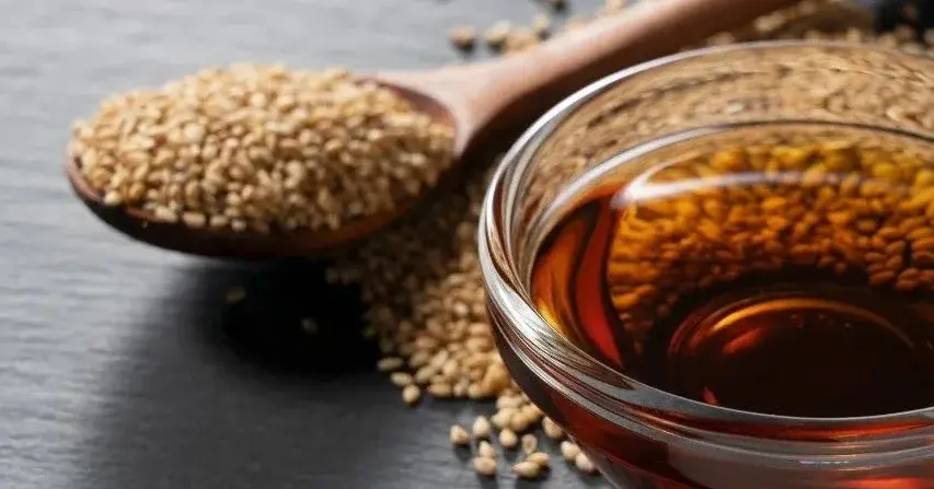 Olej sezamowy w miseczce, obok łyżka pełna ziaren sezamu.