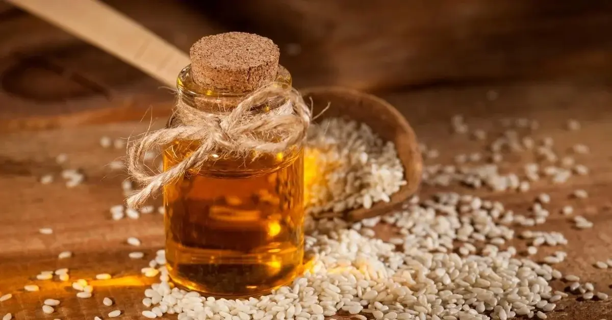 Olej sezamowy w buteleczce, obok rozsypane ziarna sezamu.