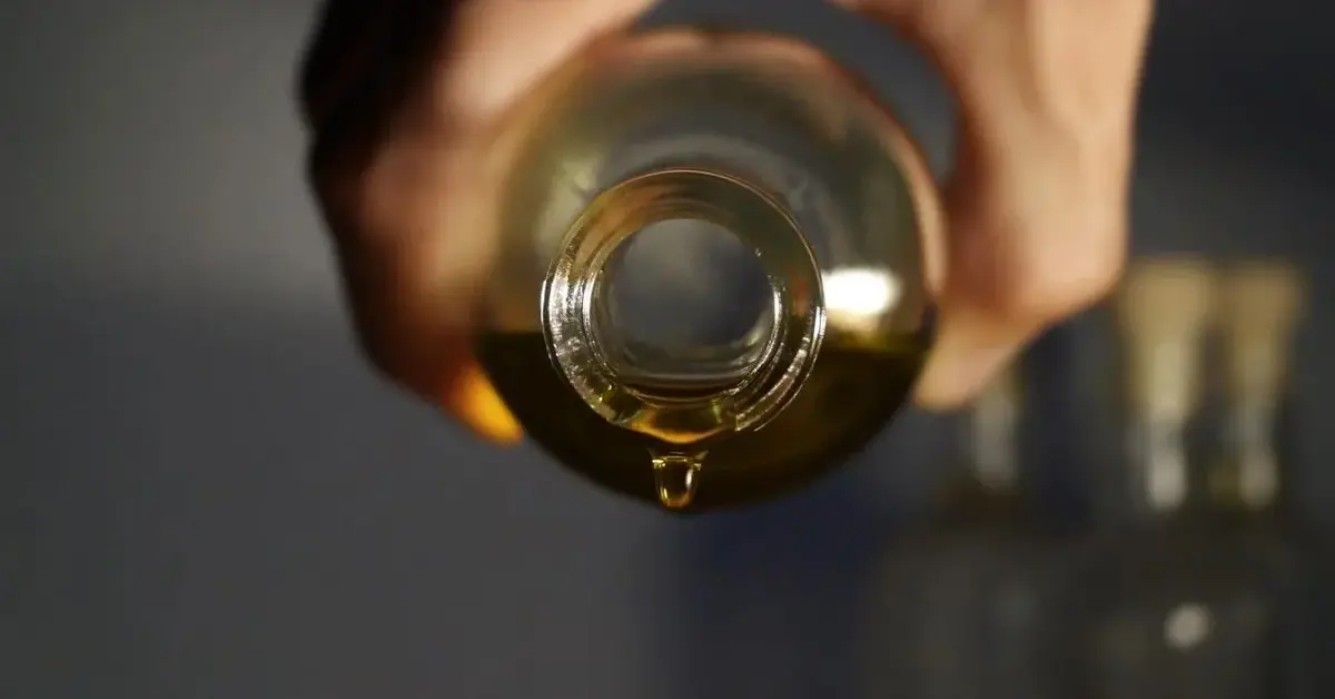 Zielony olej tamanu kapie z otwartej butelki.